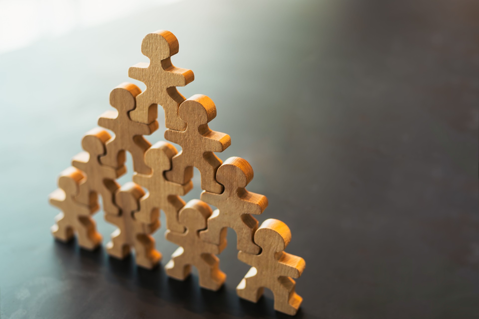 Wooden human figures forming a pyramid symbolizing teamwork, leadership, support, and organizational success. Concept of collaboration, unity, human resources, and business development.